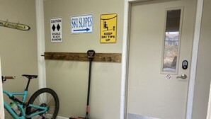 Eine Tür mit Fußmatte, ein Fahrrad, das an der Wand lehnt, und Schilder, die Skipisten und höchste Schwierigkeitsgrade kennzeichnen.