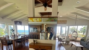 A spacious living area with a high ceiling, wooden flooring, a dining area with a large table and chairs, and a view of the ocean through large windows. - OCEANFRONT DUPLEX, with POOL, SAUNA and steps from BEACH (Hilo)