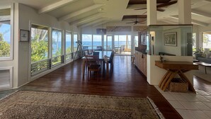 A spacious living area with a large dining table, a kitchen with a wooden countertop, and a view of the ocean through large windows. - OCEANFRONT DUPLEX, with POOL, SAUNA and steps from BEACH (Hilo)