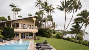 A two-story house with a pool, surrounded by palm trees and a view of the ocean. - OCEANFRONT DUPLEX, with POOL, SAUNA and steps from BEACH (Hilo)