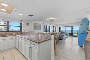 A modern kitchen with granite countertops, white cabinetry, and a view of the ocean through large windows.