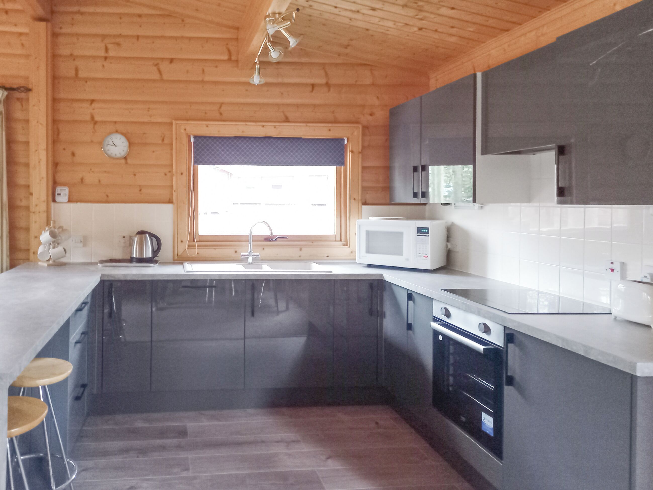 Cucina moderna con lavandino, forno a microonde e fornello, pareti in legno e finestra con persiane.