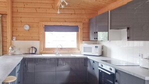 Ett modernt kök med diskho, mikrovågsugn och spis, träpanel på väggarna och ett fönster med persienner.