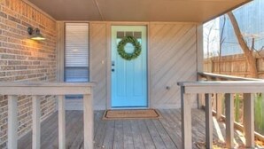 A covered porch with a blue door, a brick wall, and a wooden deck.