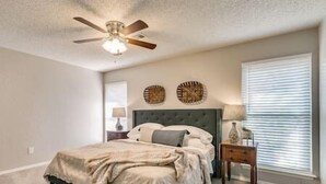 A bedroom with a bed, a nightstand, a lamp, a ceiling fan, and two wall decorations.