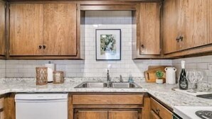 A kitchen with wooden cabinets, a white countertop, a sink, and a framed picture on the wall.