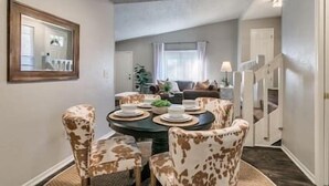 A dining area with a round table, four patterned chairs, and a mirror on the wall.