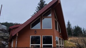 Une cabane en bois à deux étages, dotée d’un toit en pente, de grandes fenêtres et d’une terrasse entourée d’une clôture.