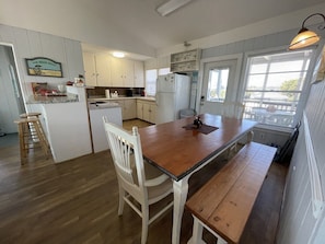 Uma cozinha com mesa e banco de madeira, armários brancos e uma janela com persianas.