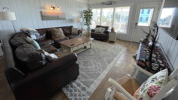 A cozy living room with a brown leather sofa, a wooden coffee table, and a white armchair. There is a large window with blinds, a potted plant, and a decorative wall hanging. - San Bel - Second row in Garden City Beach (Garden City)
