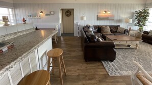 A spacious living area with a kitchen counter, a dark brown sofa, a wooden coffee table, and a ceiling fan. - San Bel - Second row in Garden City Beach (Garden City)