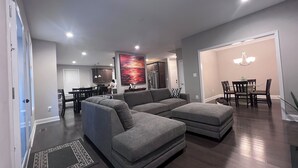 A modern living room with a sectional sofa, a dining area with a chandelier, and a kitchen in the background. - NEW 5 Bedroom Home with  Pier by Water (Riviera Beach)