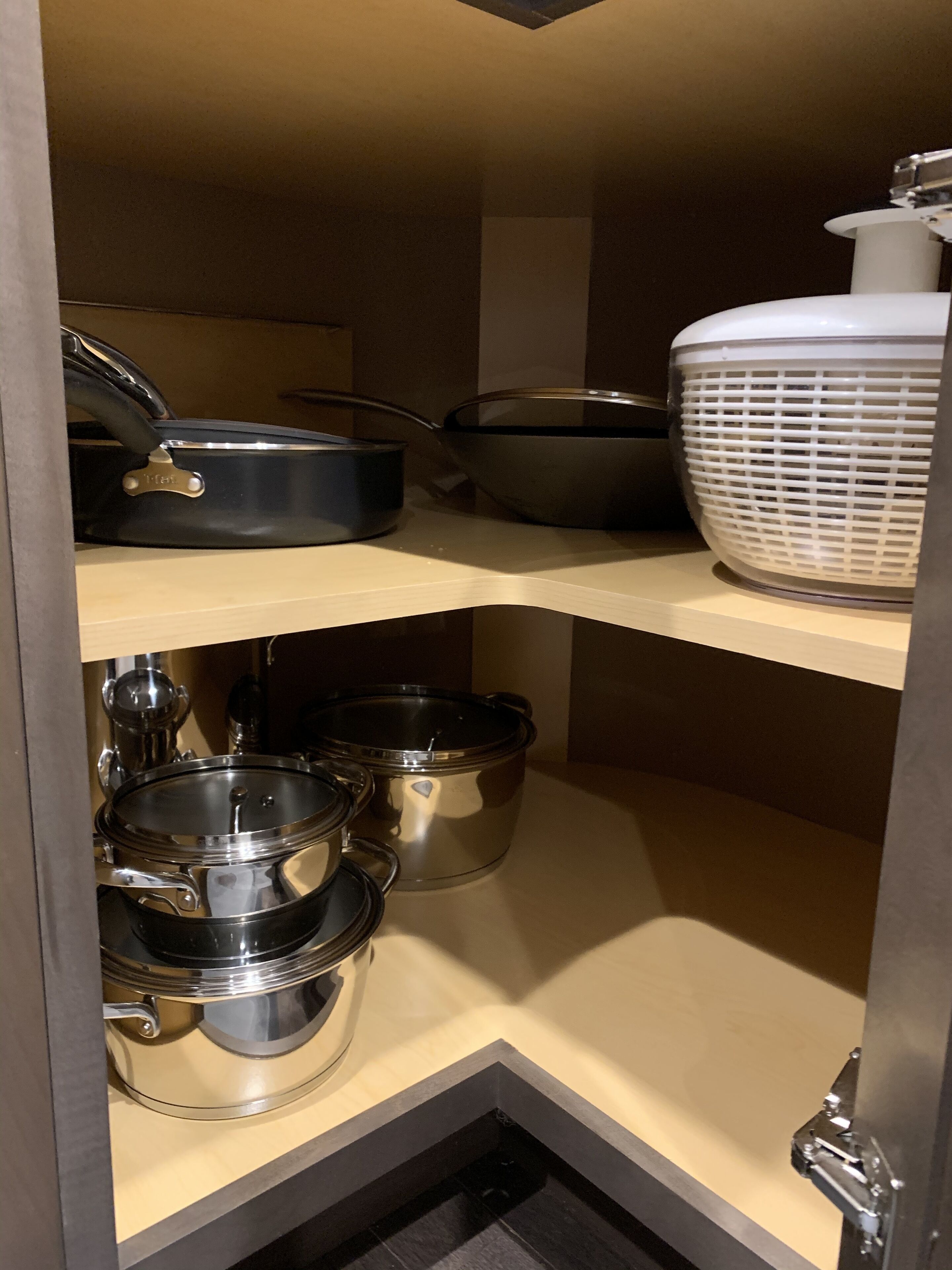 Een keuken met roestvrijstalen kookgerei op planken, waaronder potten, pannen en een rijstkoker.