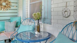 A cozy outdoor seating area with a round glass table, blue metal chairs, and teal cushions.