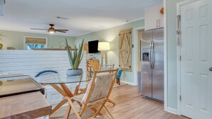 A modern kitchen with a dining area, featuring a wooden table, chairs, a refrigerator, and a ceiling fan.