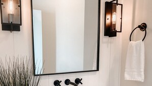 A bathroom with a white sink, wooden countertop, and a large mirror. There are two wall-mounted light fixtures and a towel rack with a white towel. - Bright stylish home minutes to downtown! New build with HUGE pool/hot tub combo! (Chattanooga)