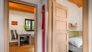 Une pièce avec un plancher en bois, un lit avec une tête de lit verte, un bureau avec une chaise et une fenêtre donnant sur un paysage verdoyant.