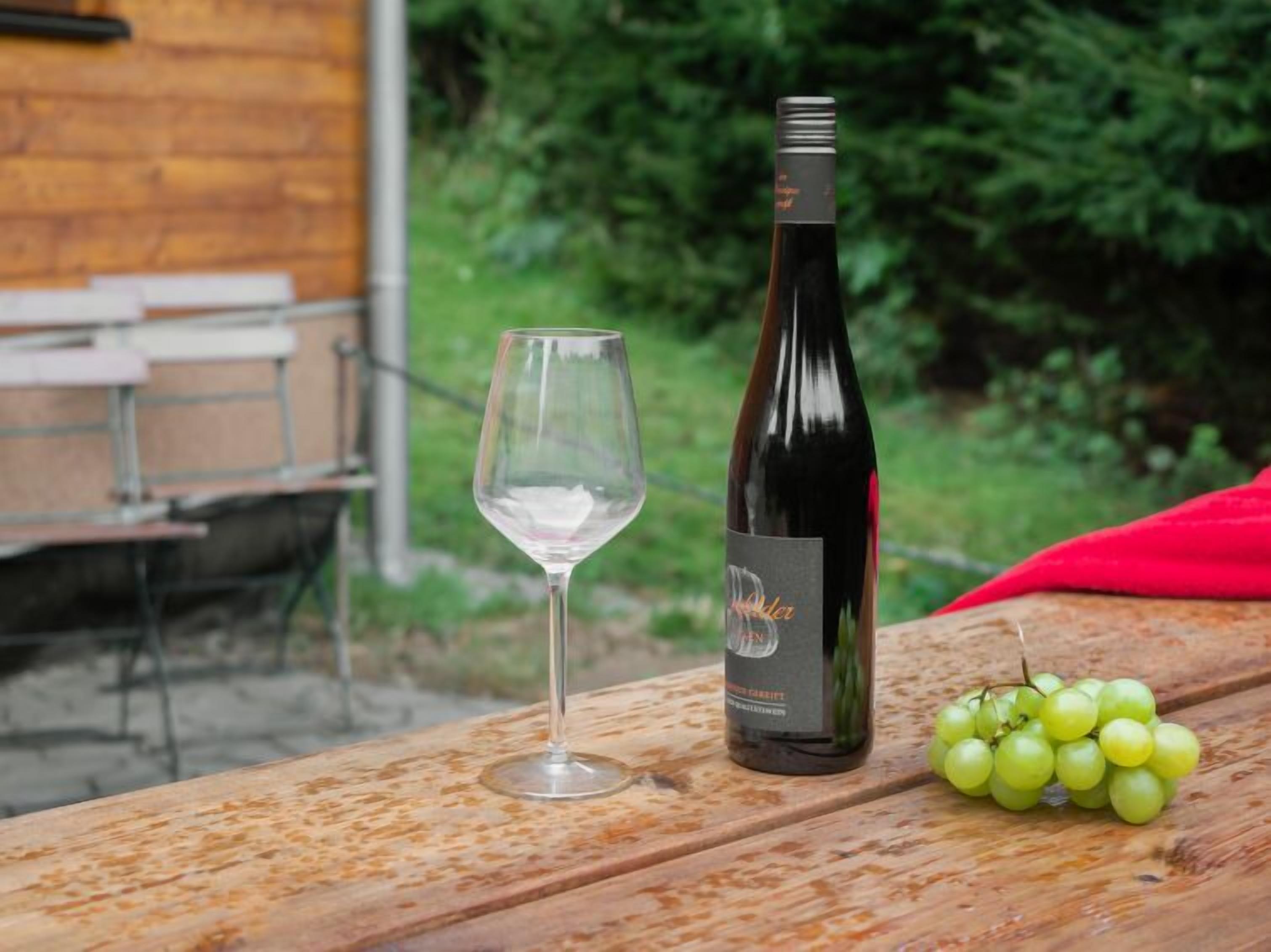Eine Weinflasche und ein Glas auf einem Holztisch, nebenan eine Traubengruppe.