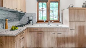 Une cuisine avec des meubles en bois, un plan de travail en marbre, une machine à café et une fenêtre donnant sur une maison.