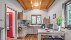 Une cuisine compacte avec des meubles en bois, une table à manger avec deux chaises, une fenêtre donnant sur un espace verdoyant et une porte rouge.