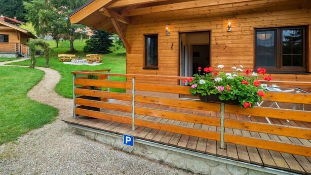 Une cabane en bois dotée d’une terrasse couverte, d’un chemin de gravier et d’un jardin agrémenté de bancs et de fleurs.