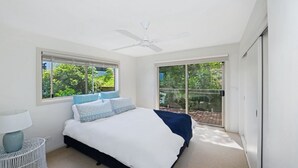 Ein Schlafzimmer mit Bett, Deckenventilator, Fenster und einer Schiebetür.
