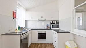 Kompakti keittiö, jossa on valkoiset kaapit, sisäänrakennettu uuni, mikroaaltouuni ja astianpesukone.