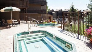 An outdoor swimming pool area with two 3 FT pools, surrounded by a fence, with a table and chairs, and a potted plant. - Downhill Den! Mountain Views, Private Patios, Outdoor Pool, 4 Hot Tubs, Pickleball Courts! (Steamboat Springs)