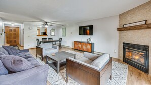 A living room with a fireplace, sofas, a coffee table, and a dining area with chairs and a table. - Lincoln Apartment w/ Balcony: 2 Mi to Loon Mtn! (Lincoln)