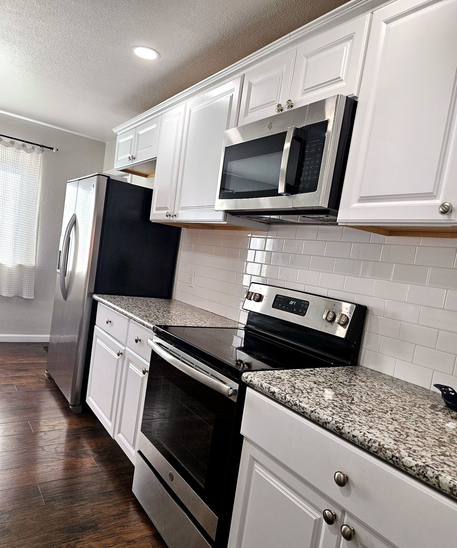 A kitchen with white cabinets, a stainless steel refrigerator, a microwave, an oven, and a granite countertop.