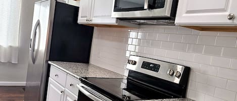 A kitchen with white cabinets, a stainless steel refrigerator, a microwave, an oven, and a granite countertop.