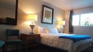 A hotel room with a bed, two bedside lamps, a chair, a framed picture on the wall, and a window with curtains.