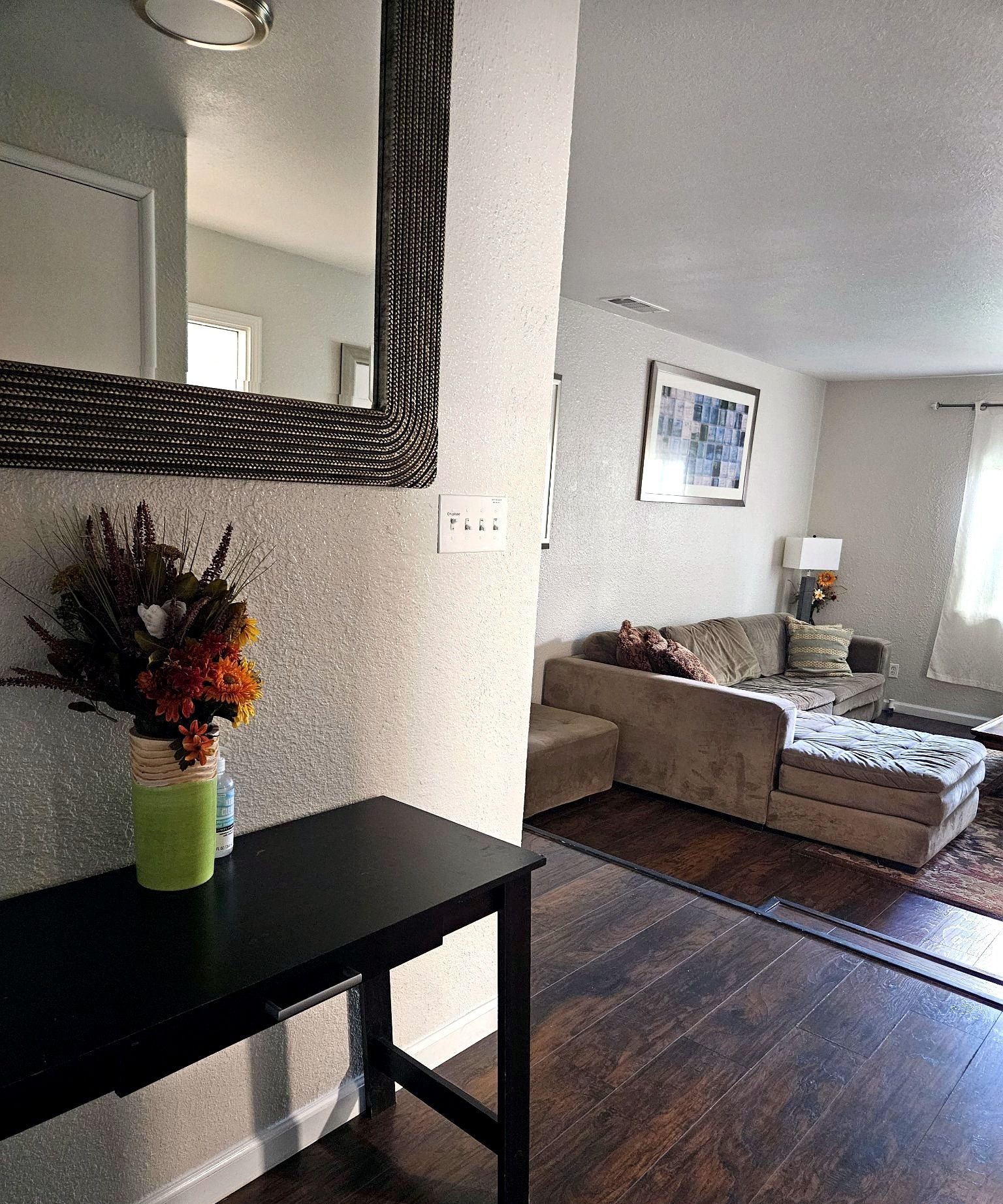 A living room with a sofa, a coffee table, a side table with a vase, and a large mirror on the wall.