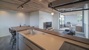 A modern kitchen with a central island, bar stools, a built-in oven, and a large window overlooking a balcony. - Shimakaji Villa Onna (Onna)