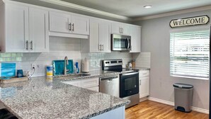 A modern kitchen with white cabinets, a granite countertop, stainless steel appliances, and a 'WELCOME' sign. - Dock & Fire Pit: Lakefront Cedar Creek Home! (Mabank)