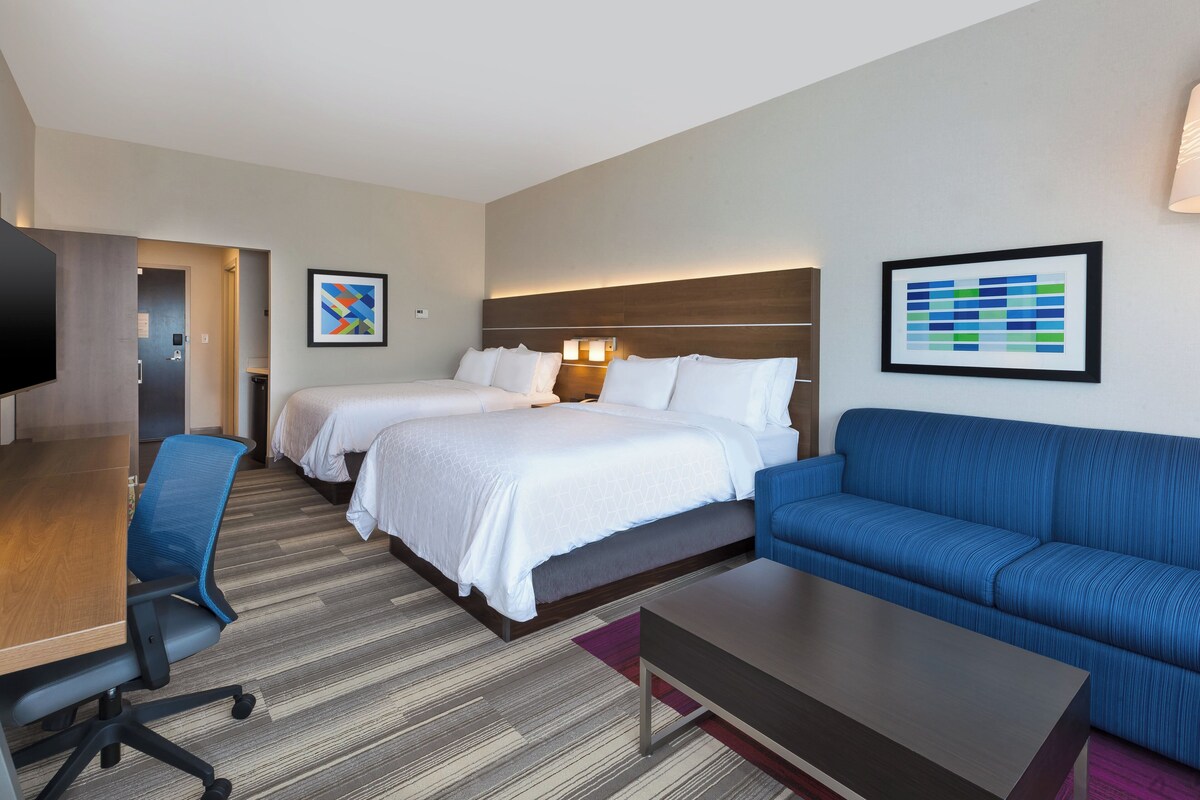 Ein Hotelzimmer mit zwei Betten, einem blauen Sofa, einem Holztisch und einem Fernseher.
