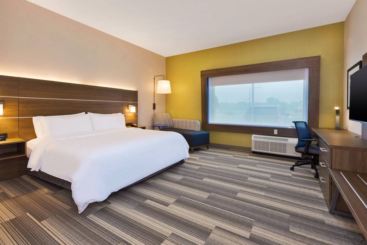 A hotel room with a large bed, a desk, a chair, a TV, and a window with a view.