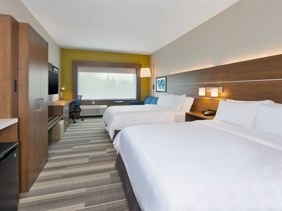 A hotel room with two beds, a desk, a chair, a TV, and a large window.
