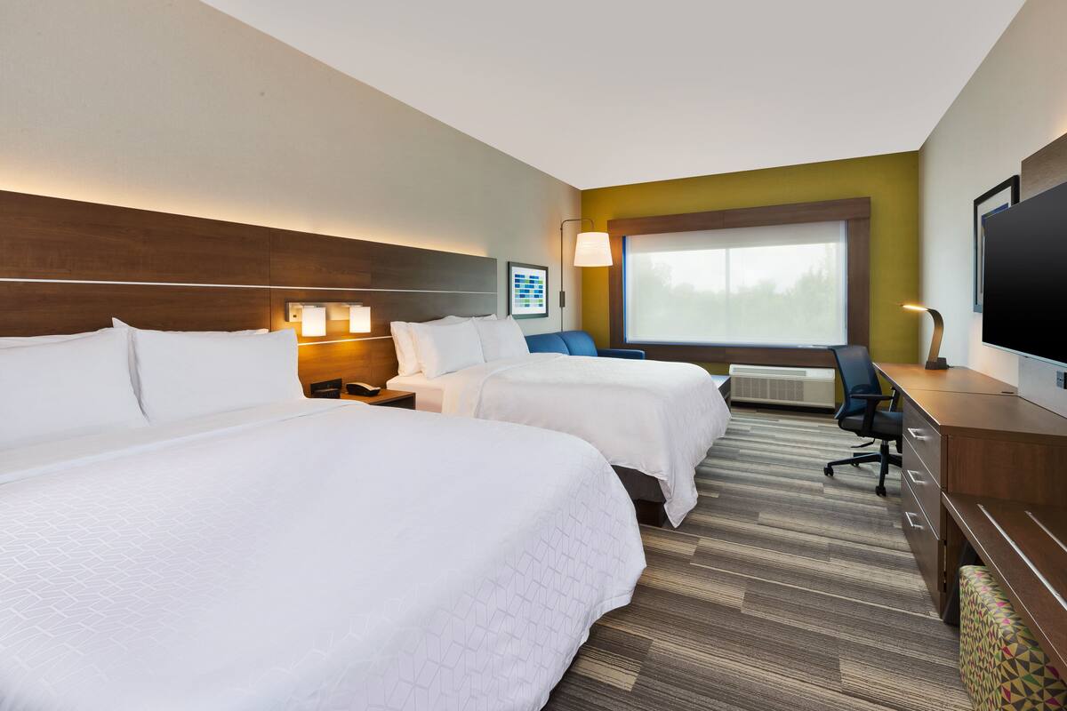 A hotel room with two beds, a desk, a chair, a TV, and a window with a view.