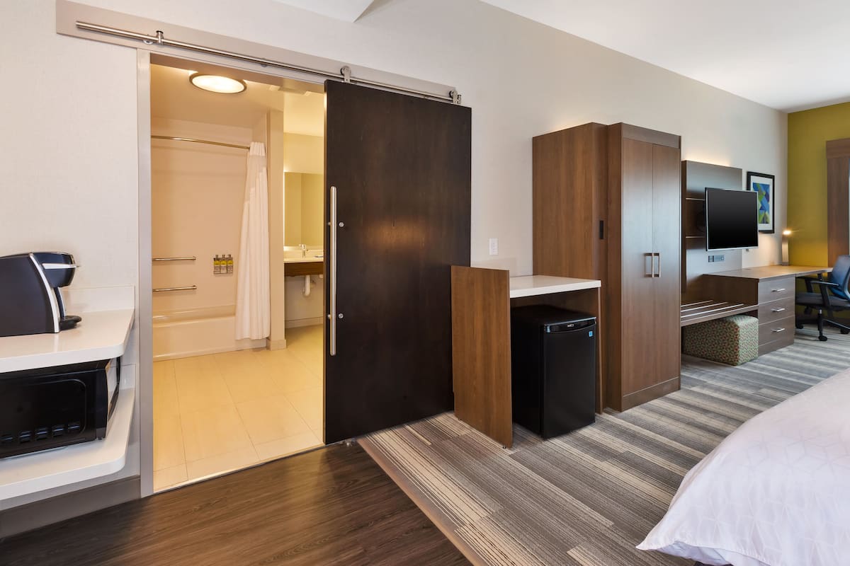 A hotel room with a sliding door to a bathroom, a desk with a chair, a bed, and a TV on the wall.