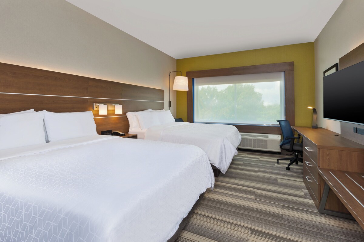 Ein Hotelzimmer mit zwei Betten, einem Schreibtisch mit Stuhl, einem Fernseher und einem großen Fenster.