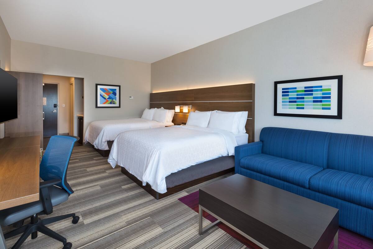 A hotel room with two beds, a blue sofa, a wooden desk, and a television.