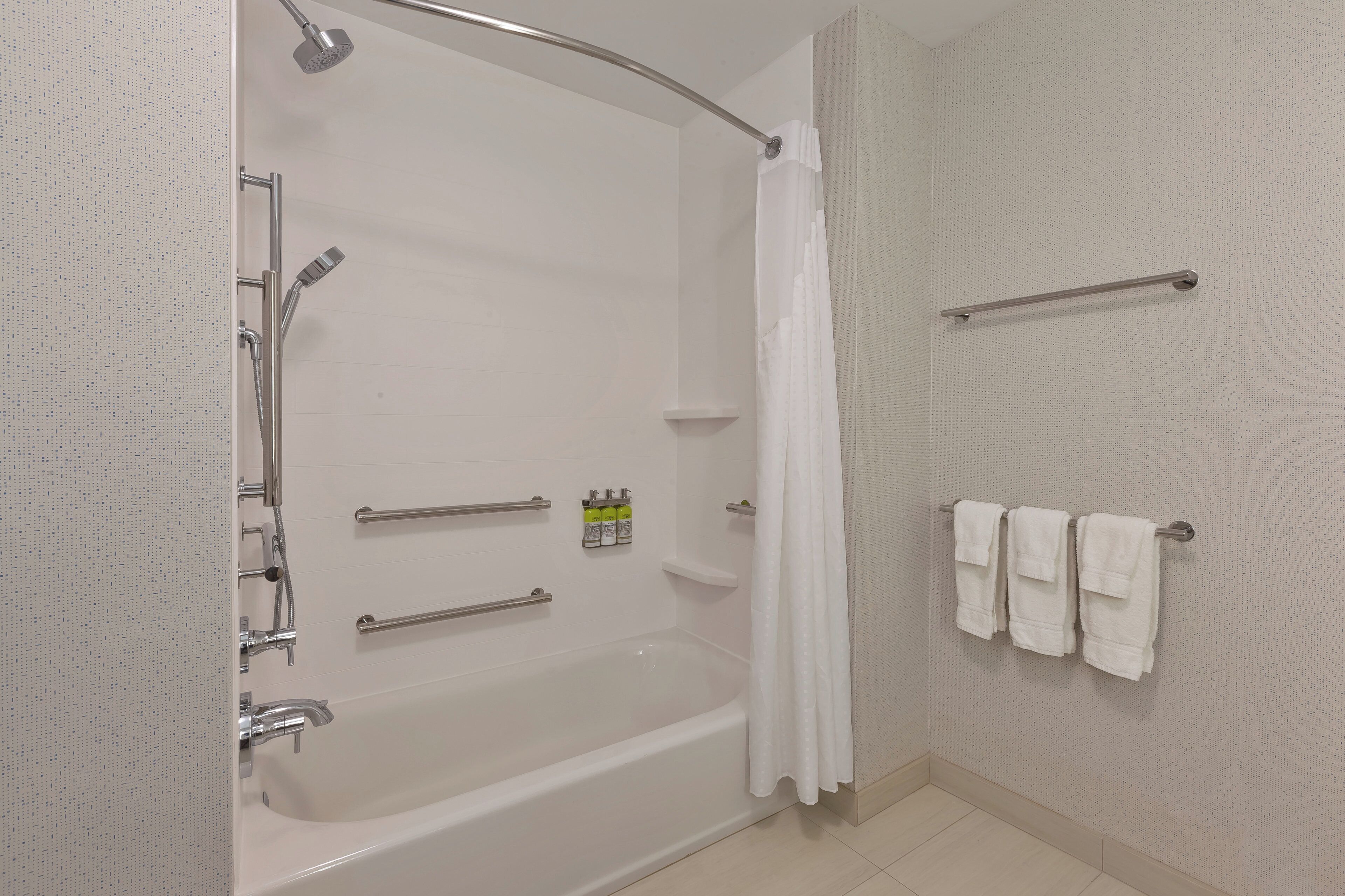 Une salle de bain équipée d’une baignoire, d’une douche, de barres d’appui, d’un porte-serviettes et d’un rideau de douche.