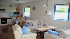 A modern living room with a sofa, a coffee table, and a dining area with a table and chairs. - Eggers, Sabine Ferienhaus (Insel Poel)