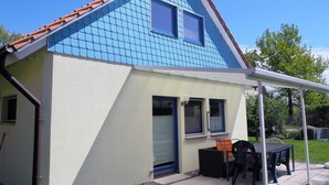 A house with a blue tiled roof, a covered patio with a table and chairs, and a small attached garage. - Eggers, Sabine Ferienhaus (Insel Poel)