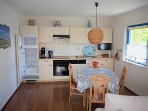 Cucina compatta con forno a incasso, macchina del caffè e microonde. È presente un tavolo da pranzo con sedie e una lampada a sospensione.