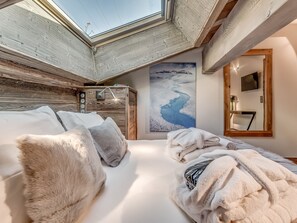 Relax in a serene bedroom with a large bed, skylight, and a painting of a snowy landscape.