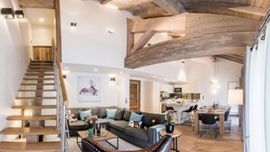 Ein geräumiger Wohnbereich mit einer Holztreppe, einer Sofagarnitur, einem Esstisch und einer Küche im Hintergrund.