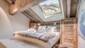 Ein Schlafzimmer mit Oberlicht, Holzbalken, einem Bett mit weißer Bettwäsche, einem Fellüberwurf und einem Holzschrank.