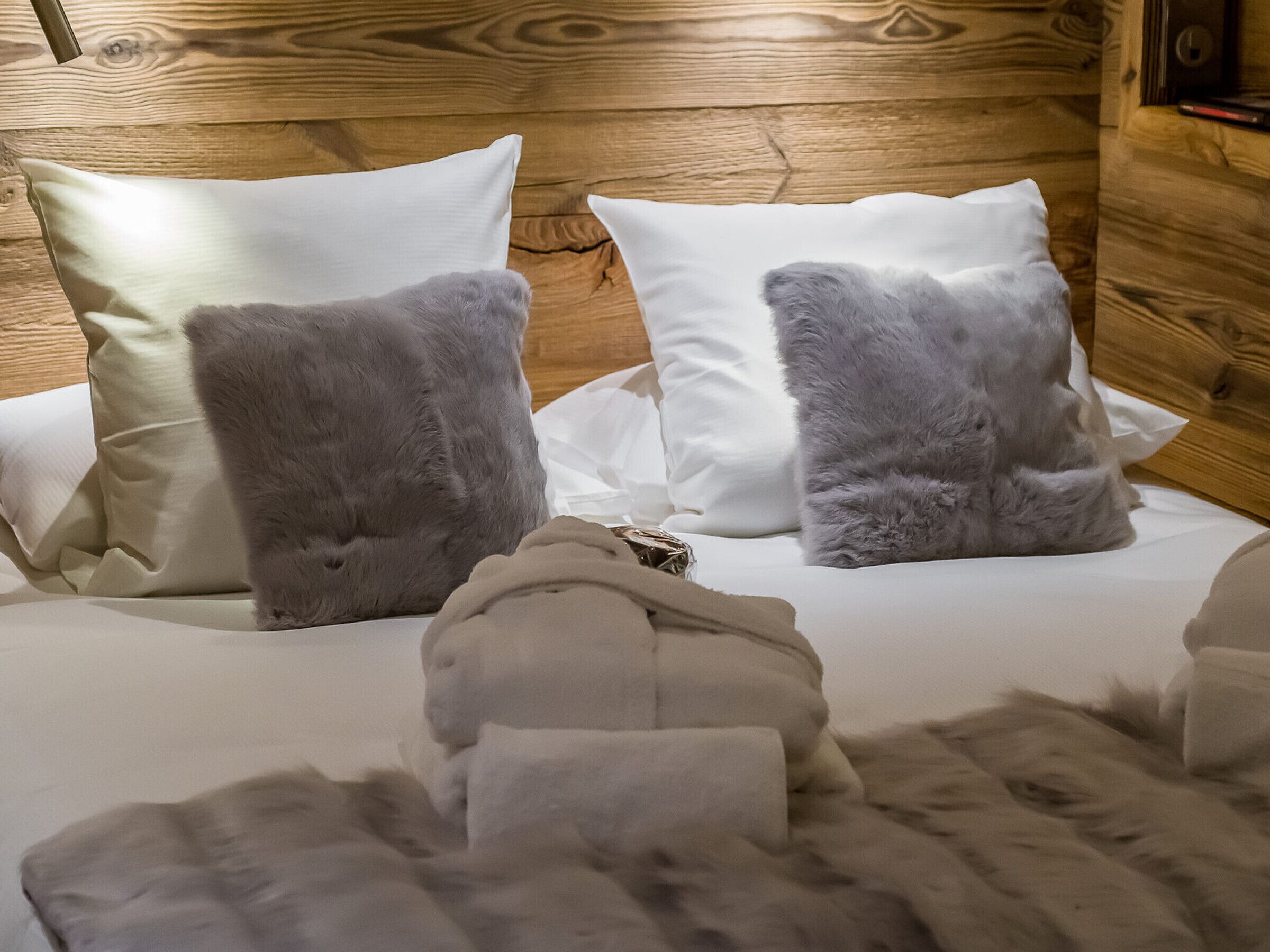 A bed with white linens and two grey fluffy pillows.